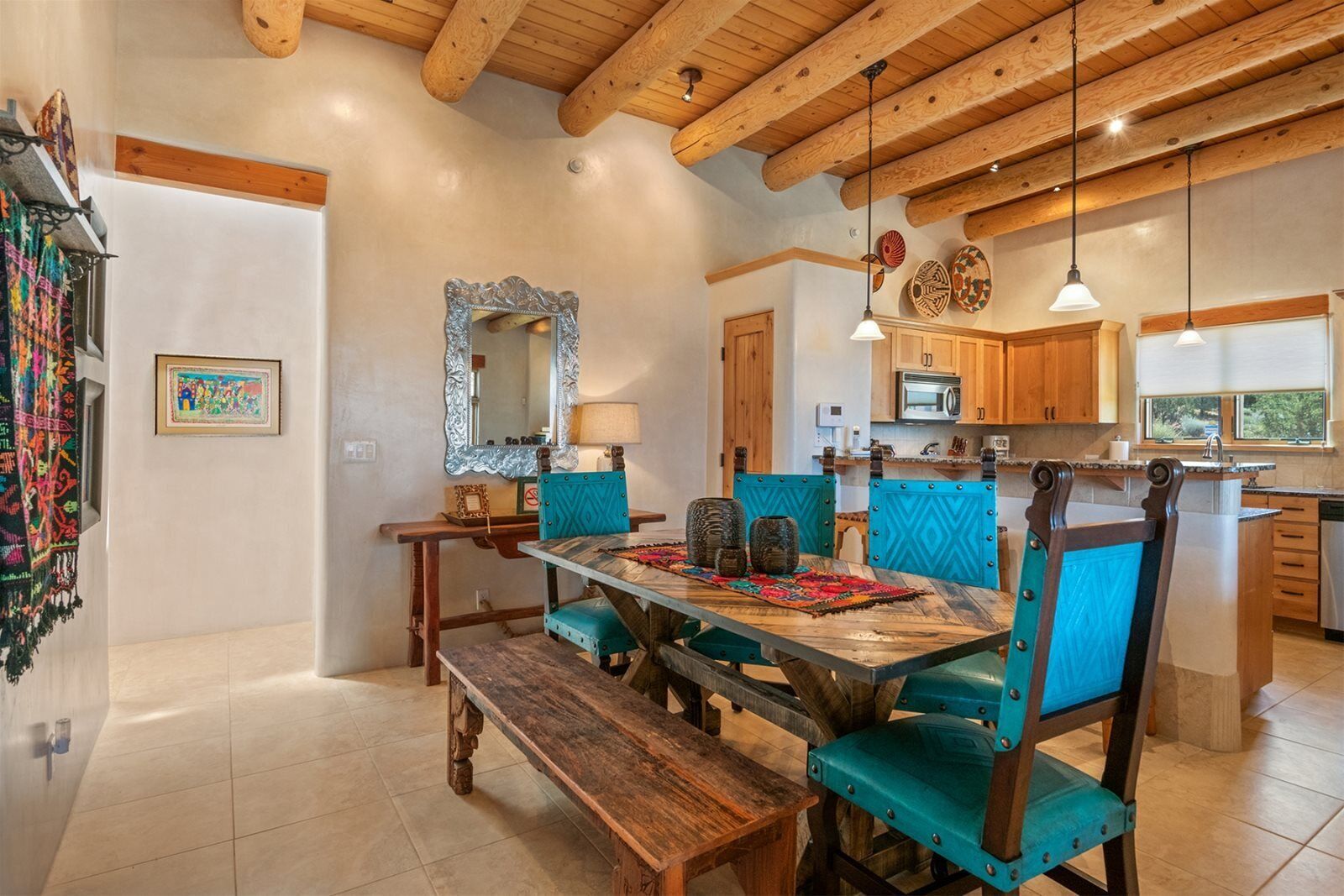 A dining area with a wooden table and chairs, a bench, a mirror, and a kitchen in the background.