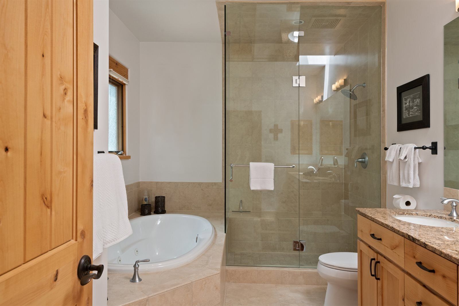 Un baño moderno con cabina de ducha de vidrio, una bañera independiente, un inodoro y muebles de madera.