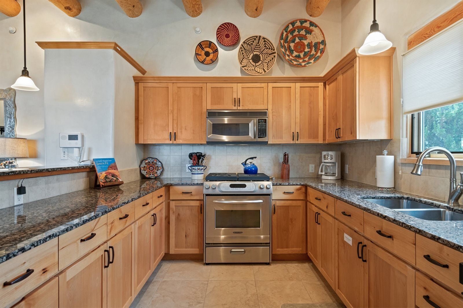 Eine moderne Küche mit Holzausbau, Edelstahlgeräten, Granitwerkplatten und dekorativen Tellern an der Wand.