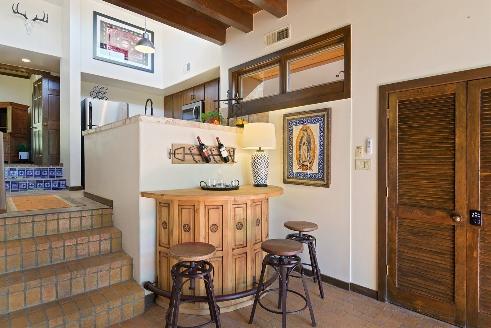 A kitchen with a wooden bar, two stools, a refrigerator, and a wine rack.