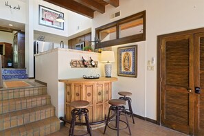 A kitchen with a wooden bar, two stools, a refrigerator, and a wine rack.