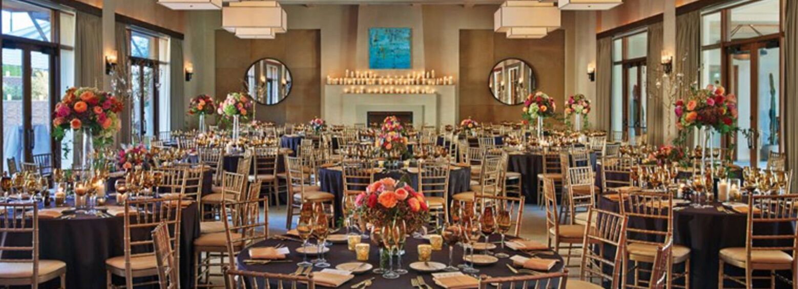 Un salón de banquetes con mesas redondas, sillas y centros de mesa florales.