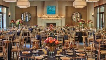 Un salón de banquetes con mesas redondas, sillas y centros de mesa florales.