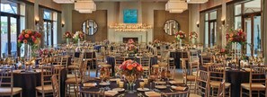 Un salón de banquetes con mesas redondas, sillas y centros de mesa florales.