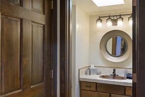 A bathroom with a wooden door, a round mirror, a sink with a towel, and a light fixture above the mirror.
