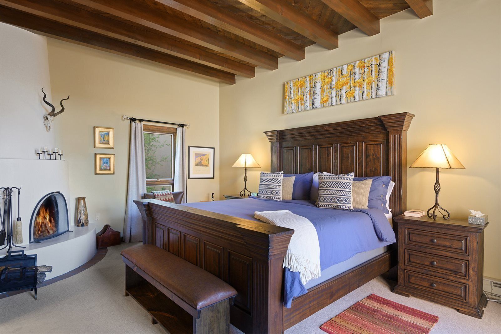 A bedroom with a wooden bed, two bedside lamps, a fireplace, and a large window.