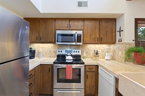 A modern kitchen with stainless steel appliances, wooden cabinets, and a tiled backsplash.