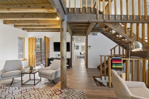 A spacious living area with a wooden staircase, two armchairs, a coffee table, and a colorful rug.