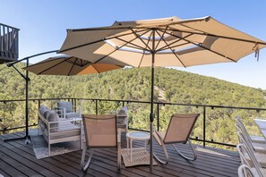 Eine Holzterrasse mit Gartenmöbeln, darunter eine Couch, Stühle und ein kleiner Tisch, unter einem großen Sonnenschirm.