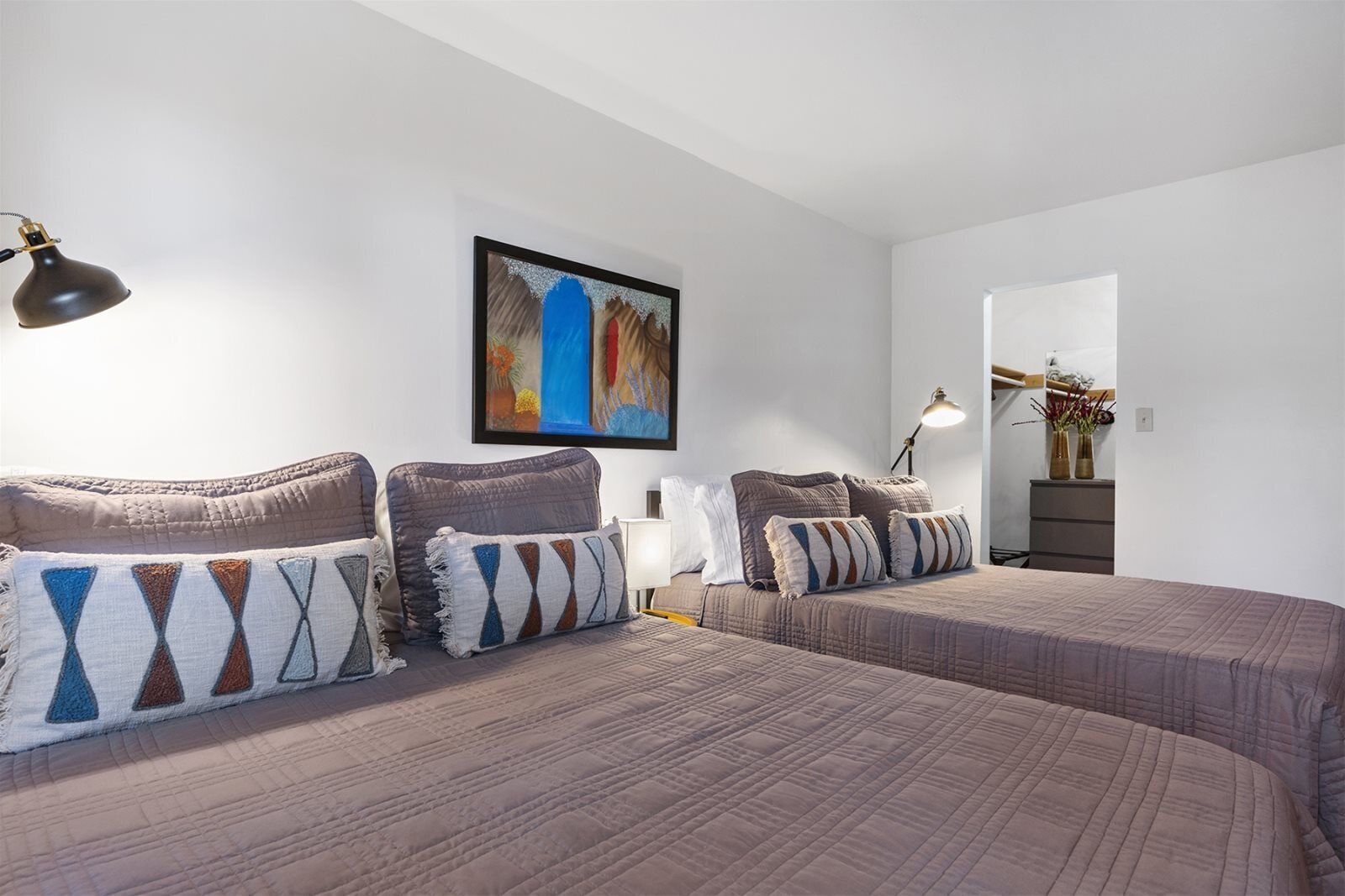 Ein Hotelzimmer mit zwei Betten, einem Bild an der Wand und einem Schreibtisch mit einer Lampe.