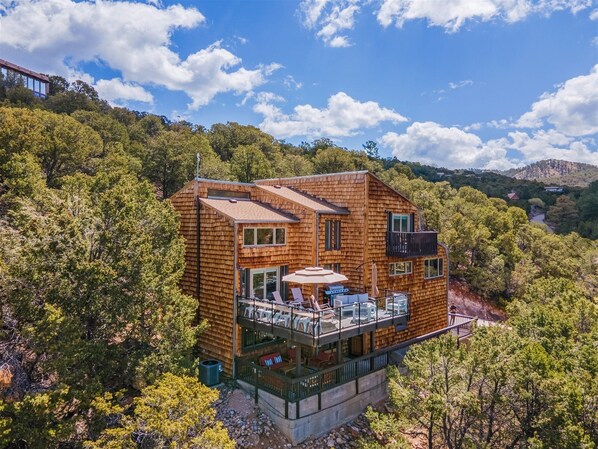 A wooden cabin with a balcony, surrounded by trees and hills.