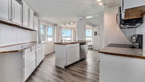 A modern kitchen with white cabinetry, a central island with a dishwasher, and a wooden countertop. - Love The 8 Lakes Life! (Pinckney)