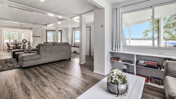 A spacious living area with a grey sofa, wooden flooring, and a bookshelf filled with board games. - Love The 8 Lakes Life! (Pinckney)