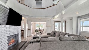 A modern living room with a fireplace, a large gray sectional sofa, and a flat-screen TV mounted on the wall. - Love The 8 Lakes Life! (Pinckney)