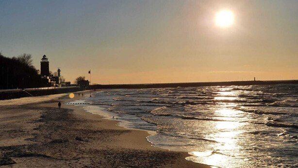 A beach with waves, a lighthouse, and a clear sky.