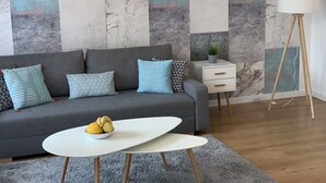 A modern living room with a grey sofa, a white side table, a small white table, and a floor lamp.