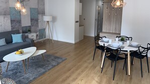 A modern living room with a grey sofa, a small white table, and a dining area with a round table and chairs.