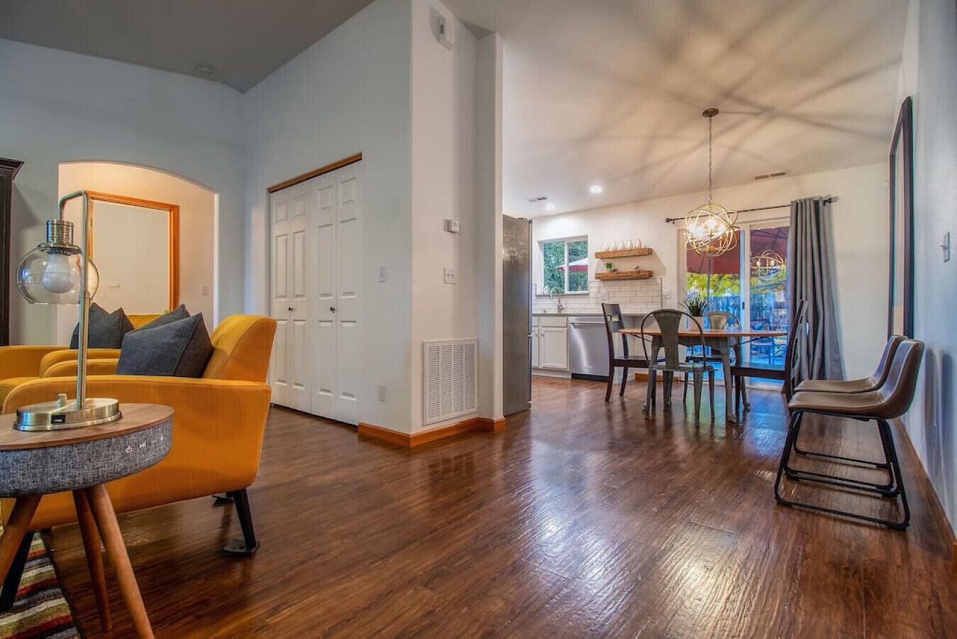 Un salon moderne avec un canapé jaune, un coin repas comprenant une table et des chaises, et une cuisine visible à travers une porte ouverte.