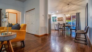 A modern living room with a yellow sofa, a dining area with a table and chairs, and a kitchen visible through an open door. - Davis House | Walk to WWU, Close to Walla Walla (College Place)