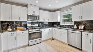 A modern kitchen with white cabinets, a granite countertop, stainless steel appliances, and a window providing natural light.