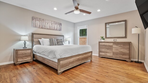 A bedroom with a wooden bed, nightstands, a dresser, a ceiling fan, and a large mirror.
