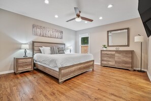 Un dormitorio con cama de madera, mesitas de noche, cómoda y ventilador de techo, además de un espejo grande.