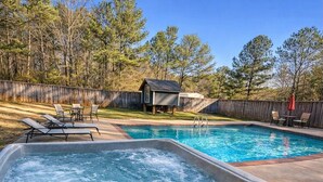 A backyard with a hot tub, a swimming pool, and a wooden deck with lounge chairs.