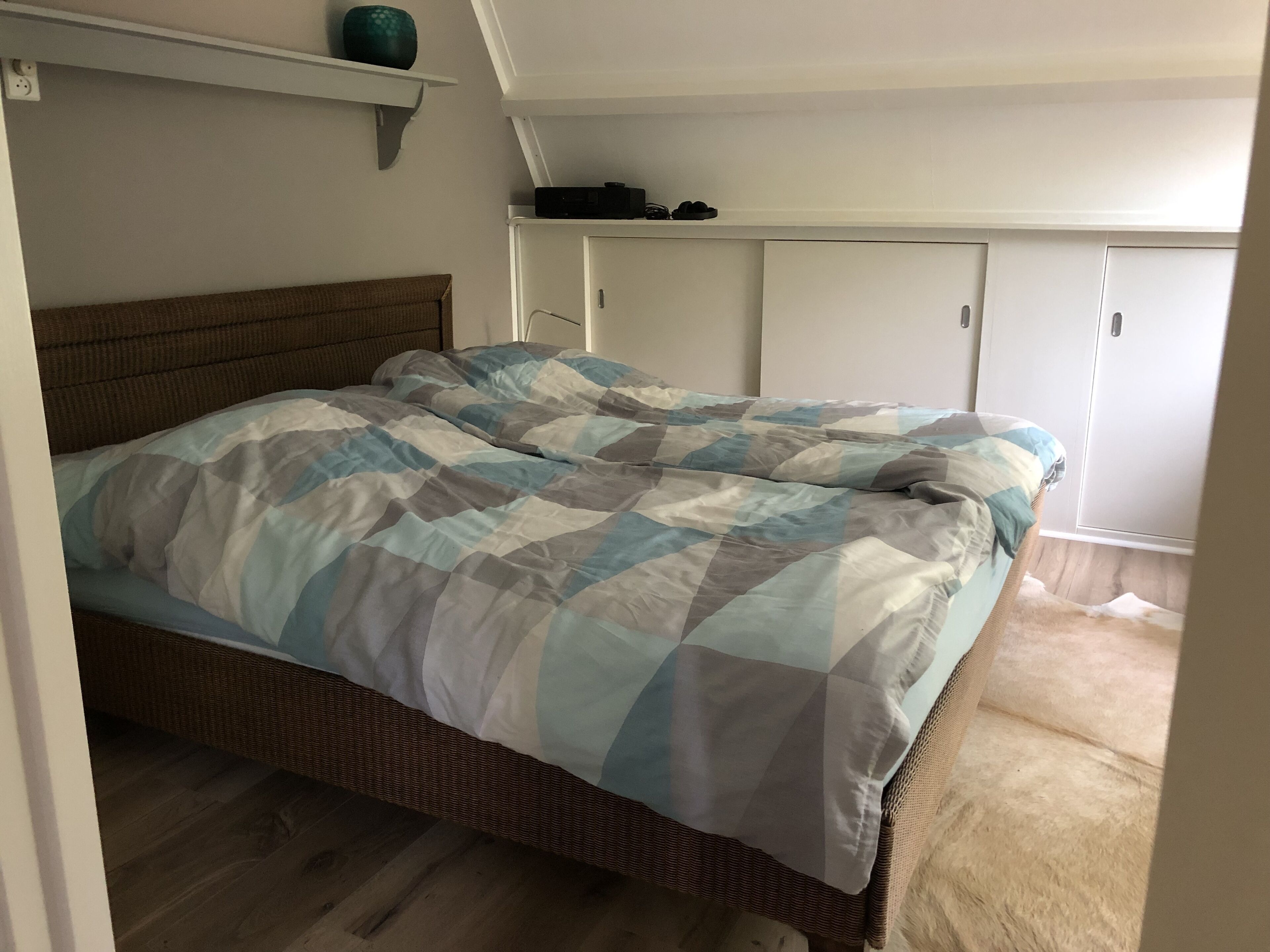 A bedroom with a bed, a shelf with a vase, and a wardrobe.