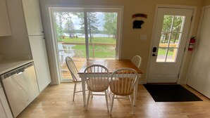 A kitchen with a wooden table and chairs, a white refrigerator, and a sliding glass door leading to an outdoor deck with a bench. - Lakeside Cottage Just Off Snowmobile/ATV Trail! (Lake Linden)