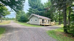 A single-story house with a gravel driveway leading to a wooden deck. - Lakeside Cottage Just Off Snowmobile/ATV Trail! (Lake Linden)