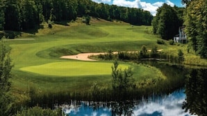 Golfkenttä, jossa on lampi, ja sen ympärillä on puita ja kirkas taivas.