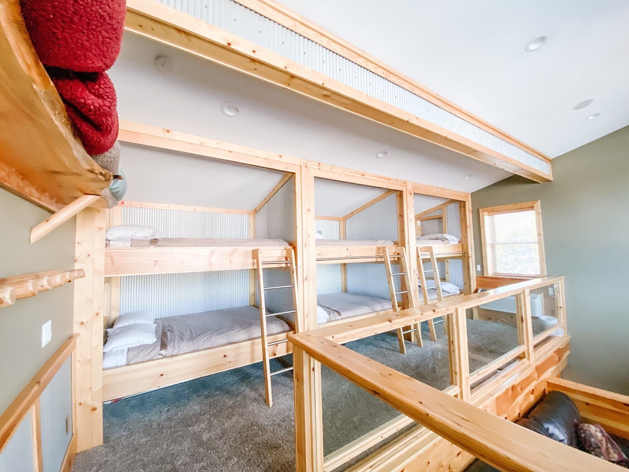 Ein Schlafraum im Schlafsaalstil mit Etagenbetten, einem Fenster und einem roten Gegenstand an der Wand.