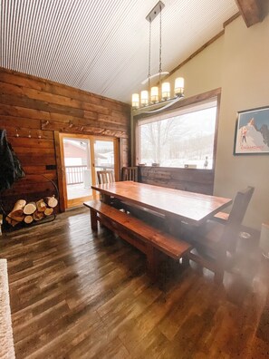 A wooden interior with a large dining table, benches, and a window with a view of a snowy landscape.