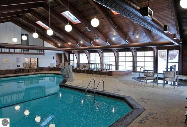 An indoor swimming pool with a wooden ceiling and large windows.