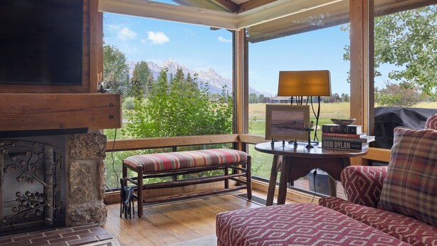 A cozy room with a fireplace, a bench, a sofa, and a table with a lamp and books. - Outpost: Golf Creek 35 - Teton Views! (Jackson)