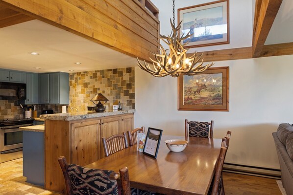 A kitchen with wooden cabinets, a stone backsplash, and a dining area with a wooden table and chairs. - Outpost: Golf Creek 35 - Teton Views! (Jackson)