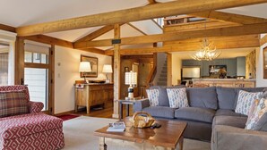 A spacious living room with a wooden ceiling, a grey sofa, a red patterned ottoman, and a wooden coffee table. - Outpost: Golf Creek 35 - Teton Views! (Jackson)