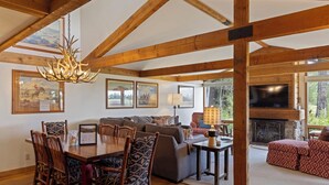 A spacious living area with a wooden ceiling, a dining table with chairs, a sofa, a fireplace, and framed artwork on the walls. - Outpost: Golf Creek 35 - Teton Views! (Jackson)