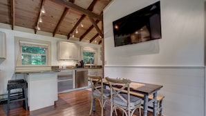 A modern kitchen with wooden beams, a dining area with a wooden table and chairs, and a flat-screen TV mounted on the wall.