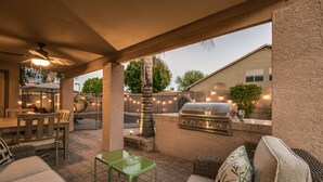 An outdoor patio area with a grill, seating, and string lights. - Sunshine and Good Times! Massive 5/bdrm with Pool, Hot Tub, and Game Room!  (Gilbert)