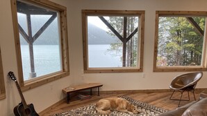 Una habitación con ventanas amplias, una guitarra, un perro, un banco y un sofá de cuero.