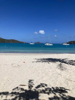 Une plage de sable blanc, avec une eau d’un bleu limpide et des voiliers.