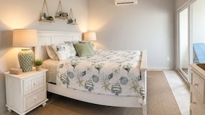 Ein Schlafzimmer mit einem Bett, Nachttischen, einer Wand-Klimaanlage und einem Fenster.