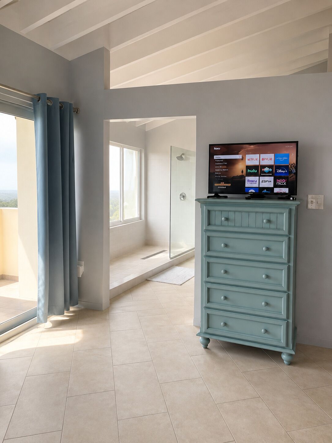 Une chambre avec un téléviseur posé sur une commode, une douche et une vue sur l’extérieur.