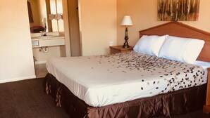 A hotel room with a large bed, a nightstand with a lamp, a dresser, and a mirror. - Hallmark Inn and Suites (Killeen)