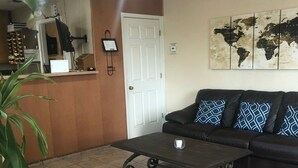 A living room with a black leather sofa, a coffee table, and a world map on the wall. - Hallmark Inn and Suites (Killeen)
