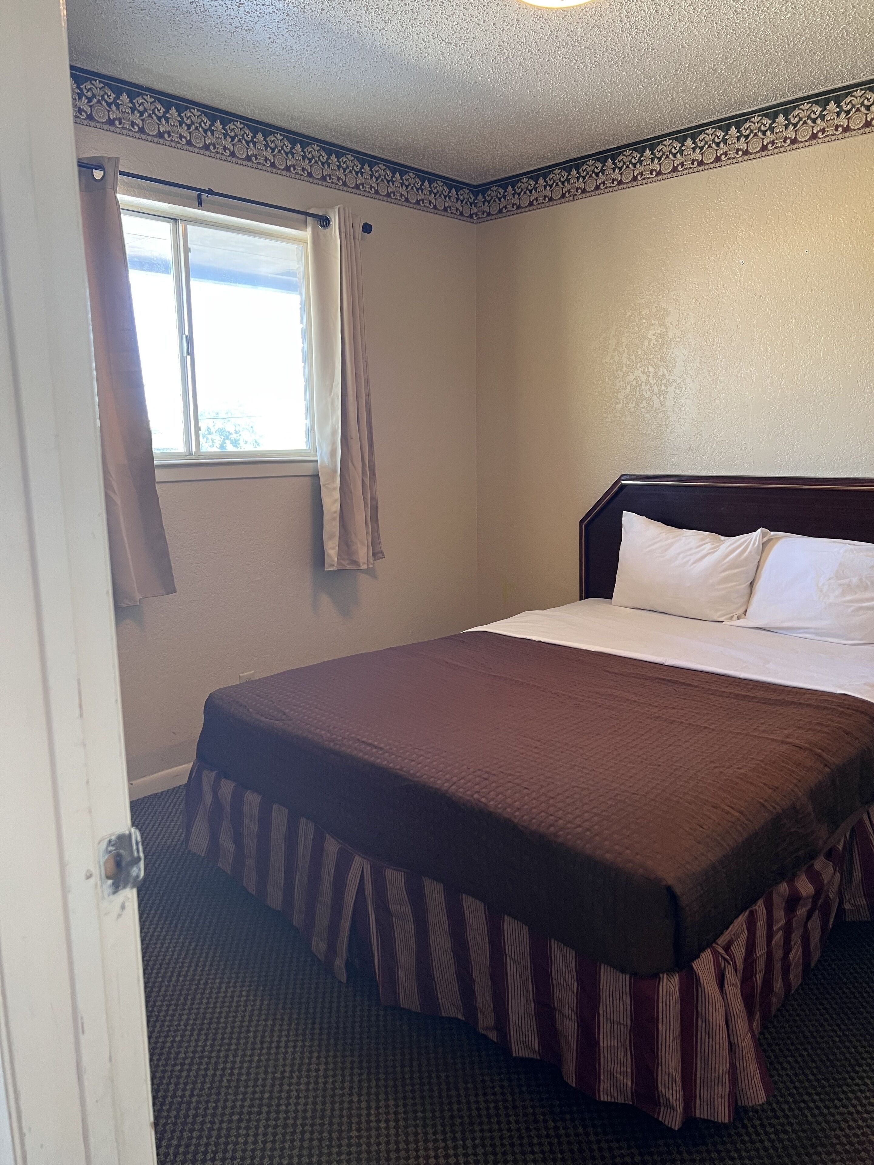 Un cuarto de hotel con una cama grande, una ventana con cortinas y un borde decorativo en el techo.