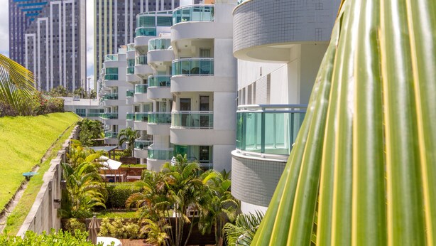 A modern hotel with multiple balconies, lush greenery, and a view of surrounding high-rise buildings. - Apart térreo no In Mare Bali Cotovelo (Parnamirim)