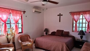 A bedroom with a bed, two chairs, a ceiling fan, and a cross on the wall. - 114Night Sep/Oct Ocean Beach Front 2 Bedrooms Villa Cozumel Snorkel Scuba Diving (Cozumel)