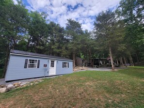 A small, single-story cabin with a front porch, surrounded by trees and a grassy area. - Glamping Clear Spring Maryland 
3-Cabin Campground (Clear Spring)